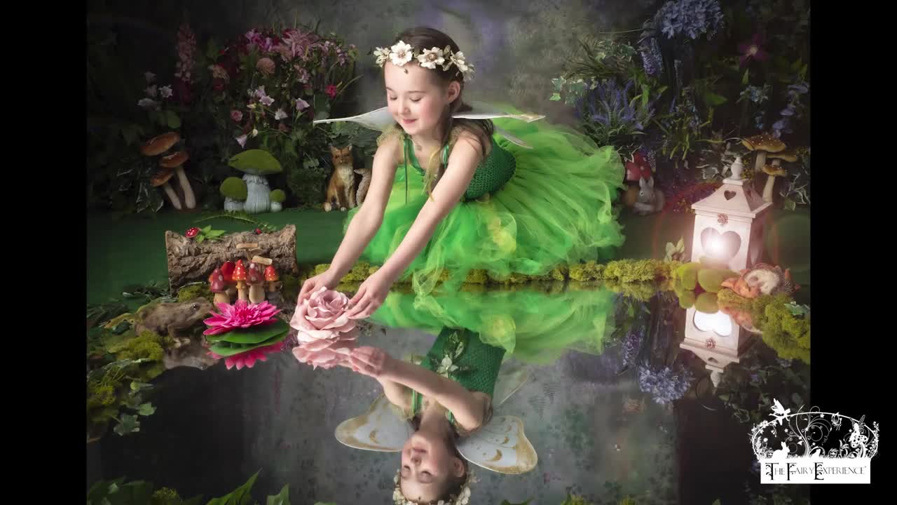 A child in a green fairy costume posing beside the woodland pool