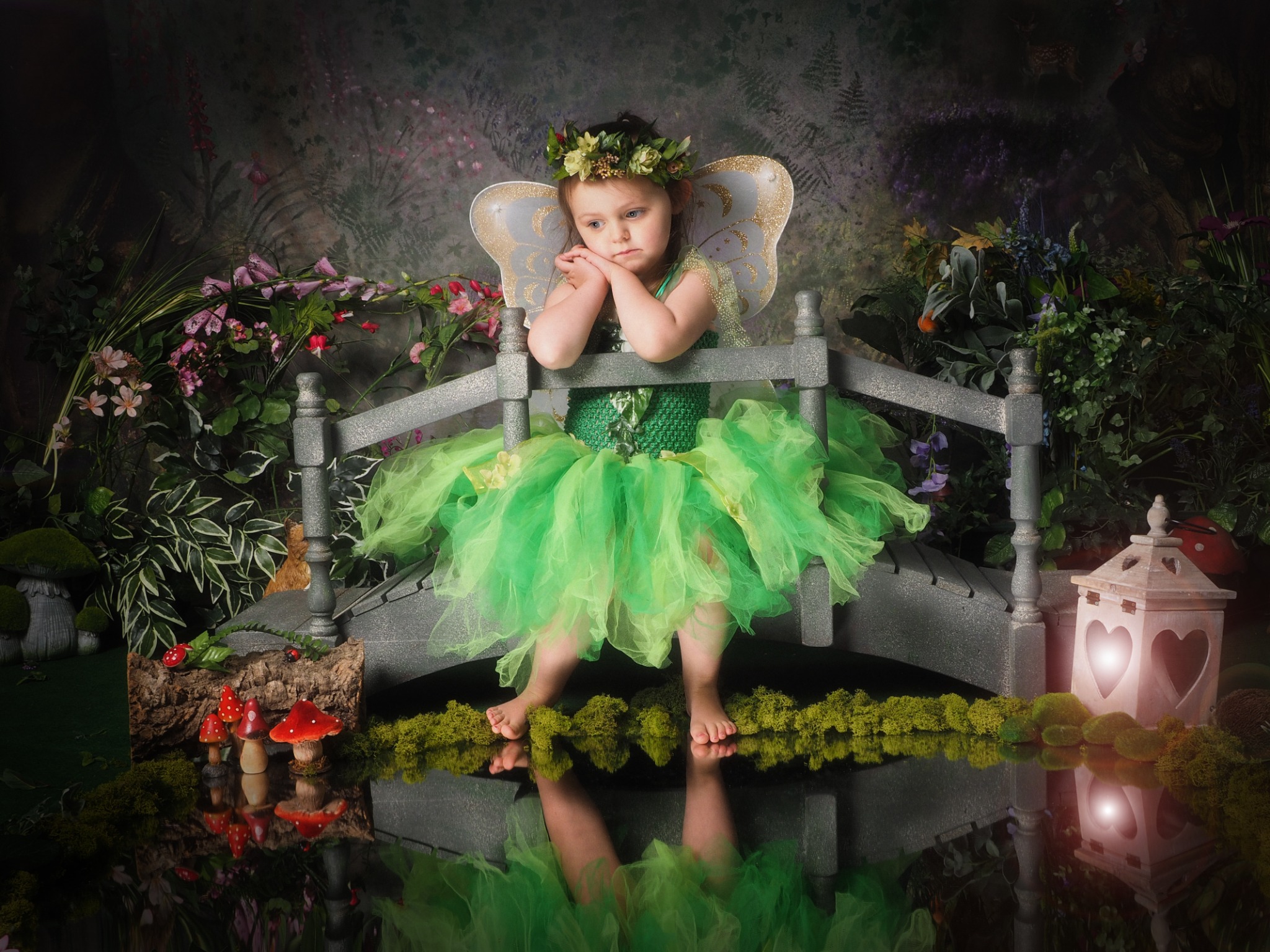 A fairy in green rests on a little woodland bridge