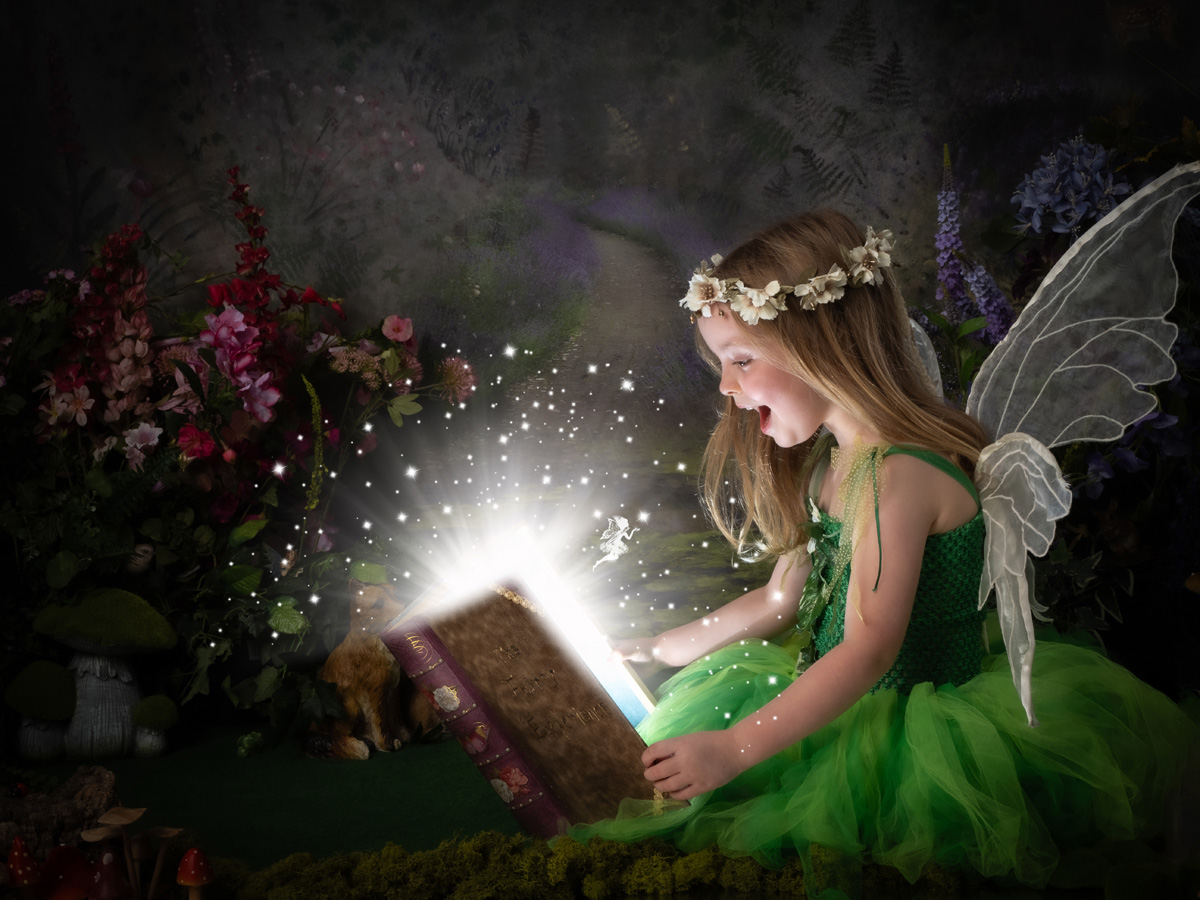 A child in a green fairy dress discovers a glowing book in a woodland portrait