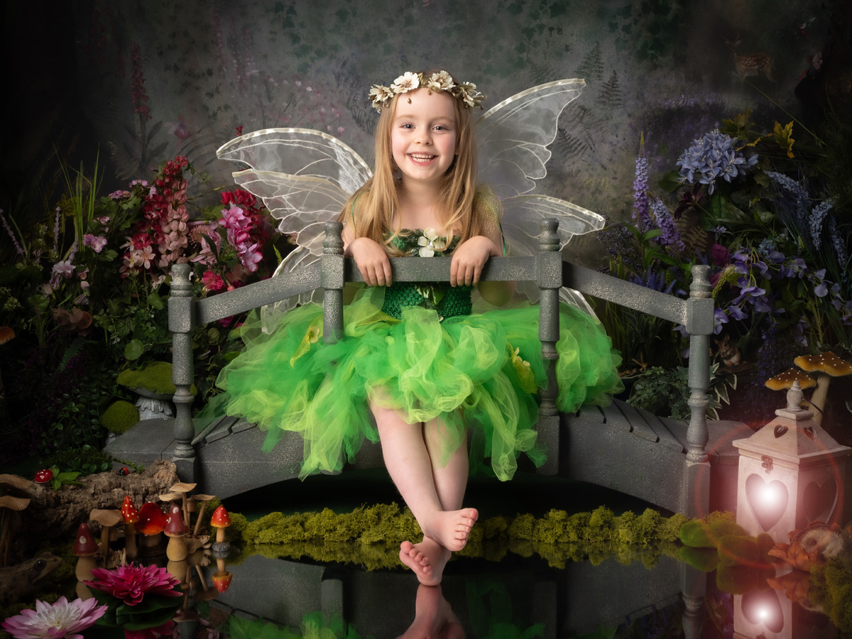 A child in green fairy wings seated on a bridge