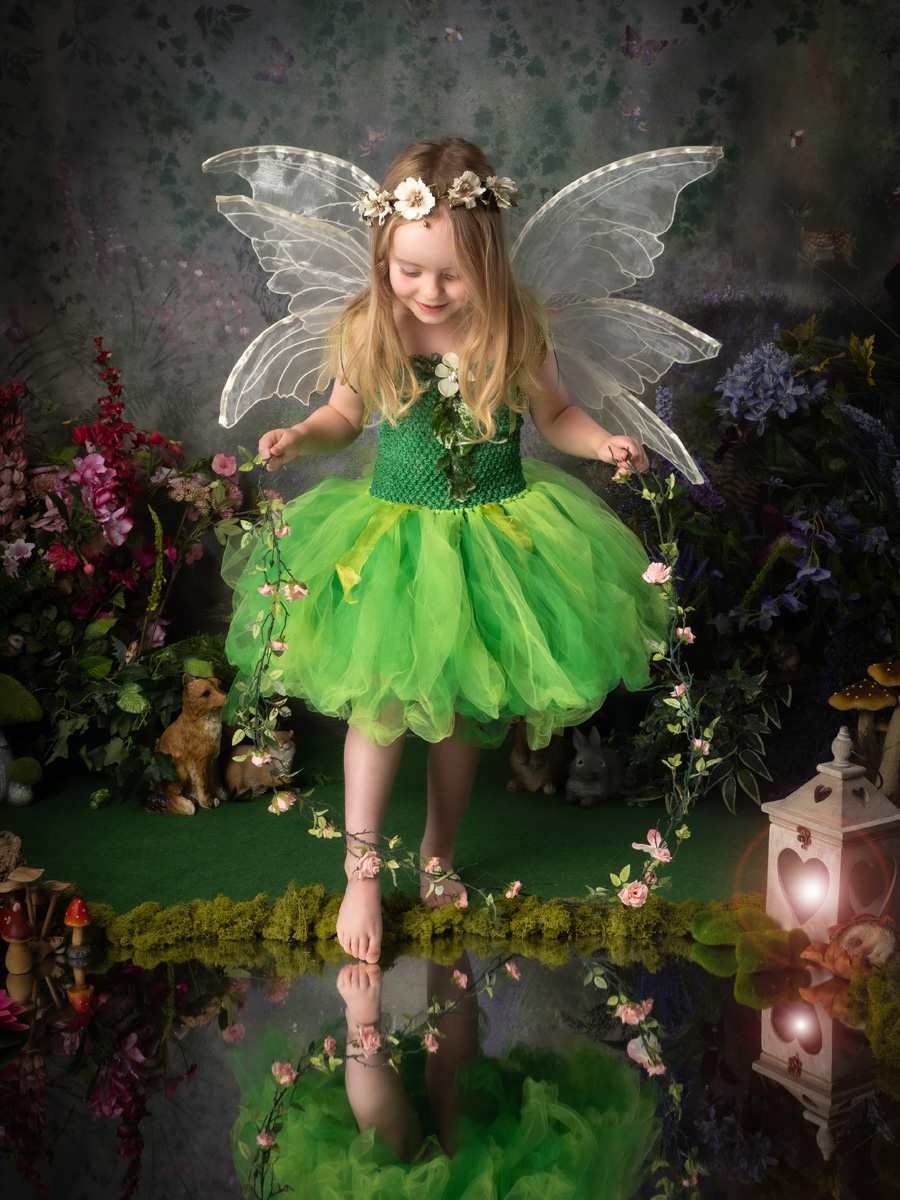 A green fairy standing beside flowers and a lantern